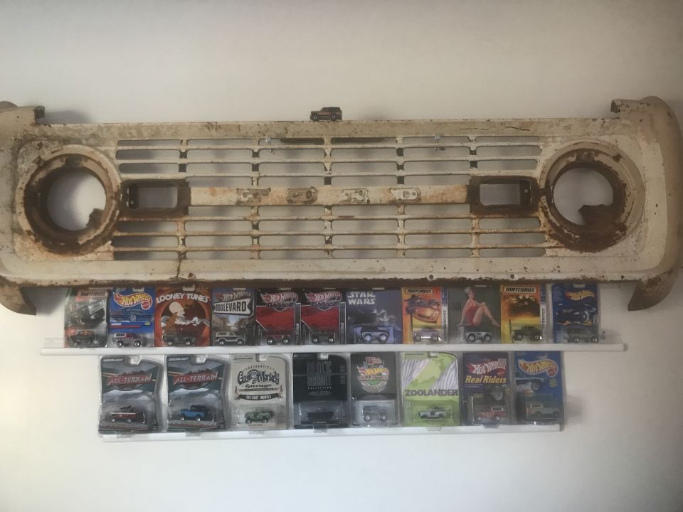 Rusty 1974 Ford Bronco grille mounted above shelves displaying collectible toy cars