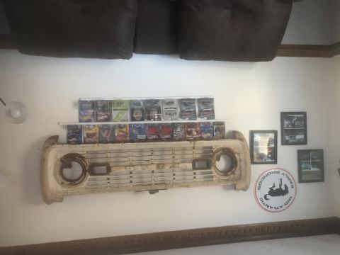 1974 Ford Bronco - A vintage Ford Bronco grille is displayed on a wall, flanked by shelves filled with collectible toy vehicles.