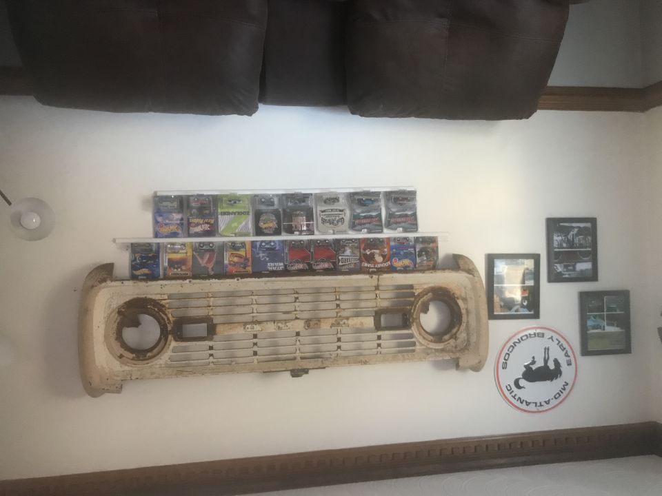 Old Ford Bronco grille mounted on wall above shelves of toy cars