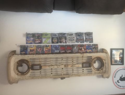 1974 Ford Bronco - A vintage Ford Bronco grille is displayed on a wall, adorned with a collection of toy cars.