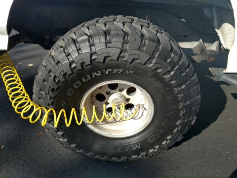 1992 Ford Bronco - A close-up view of a vehicle's tire and wheel assembly, with a yellow coiled air hose connected to the valve stem.
