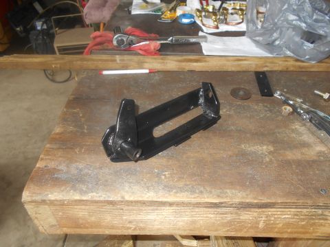 1992 Ford Bronco - A black metal bracket sits on a workbench next to tools and other parts.