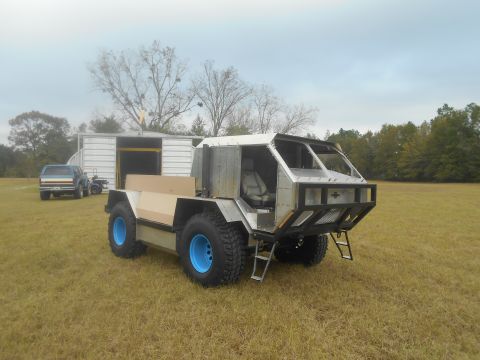 1992 Ford Bronco - Custom off-road vehicle with large blue wheels and a metal body, parked in a grassy field.