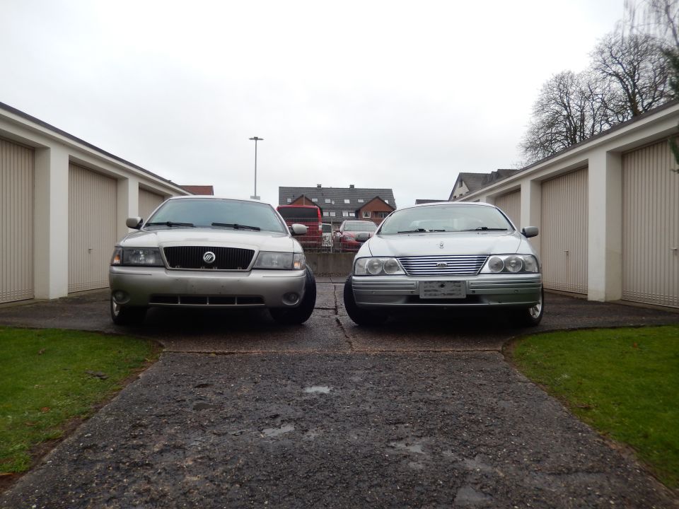 Silver sedan with a chrome grille and round headlights parked in front of garages