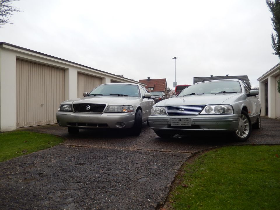 Silver Mercury Grand Marquis and a silver Ford sedan parked in front of garages