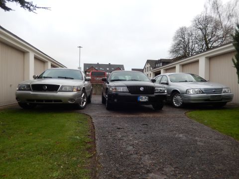 1999 Ford Fairlane - Three sedans are parked in a driveway between garages on an overcast day.