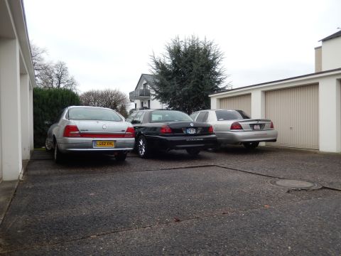 1999 Ford Fairlane - Three sedans are parked in a driveway in front of a residential building with garages.