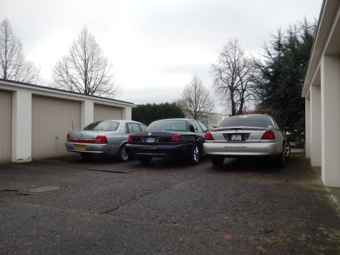 1999 Ford Fairlane - Three sedans, including a Mercury Marauder, are parked in front of garages on an overcast day.