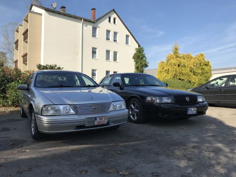1999 Ford Fairlane - Two sedans, a silver Ford and a black Mercury, are parked side-by-side on a sunny day.