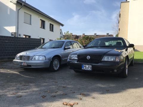 1999 Ford Fairlane - Two sedans, a black Mercury Grand Marquis and a silver Ford, are parked outdoors on a sunny day.
