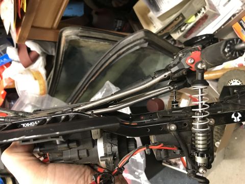 1989 Ford Bronco - Close-up of an RC car's chassis and suspension system, with a hand visible.