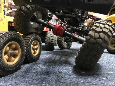 1989 Ford Bronco - Multiple RC rock crawler chassis and wheels are shown from a low angle on a blue carpet.