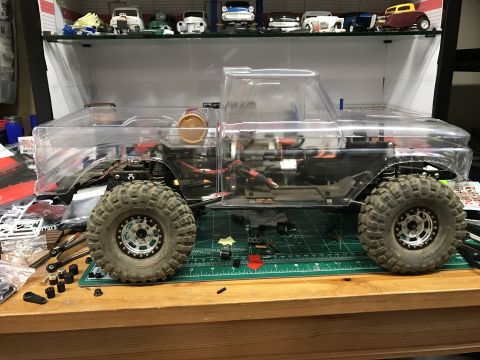 1989 Ford Bronco - A clear-bodied RC truck model sits on a workbench with various parts scattered around.