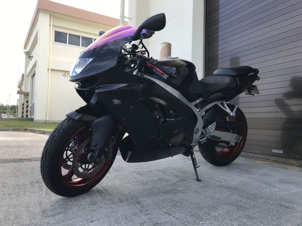 Black motorcycle with purple windshield, red rims, and a side stand deployed