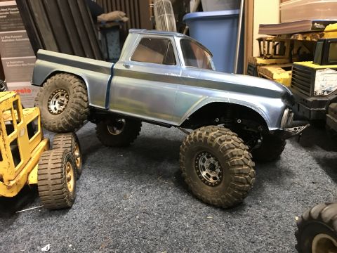 1989 Ford Bronco - A remote-controlled pickup truck with off-road tires is parked next to a yellow toy construction vehicle.
