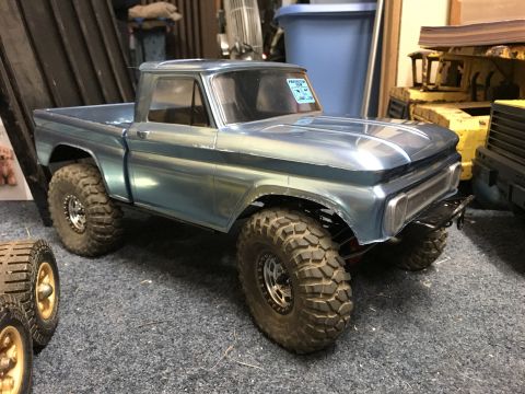 1989 Ford Bronco - A blue toy pickup truck with oversized tires sits on a carpeted floor next to other toys and equipment.