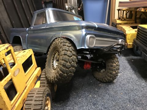 1989 Ford Bronco - A blue pickup truck model with oversized tires is parked next to a yellow toy vehicle.