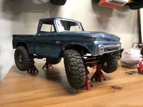 1989 Ford Bronco - A model of a blue pickup truck is displayed on red jack stands, its off-road tires and custom bumper.