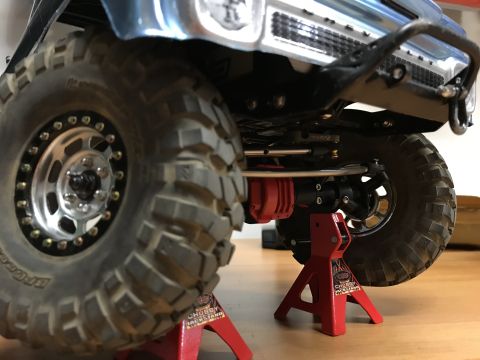 1989 Ford Bronco - Close-up view of a model vehicle's suspension and off-road tire, elevated on red jack stands.