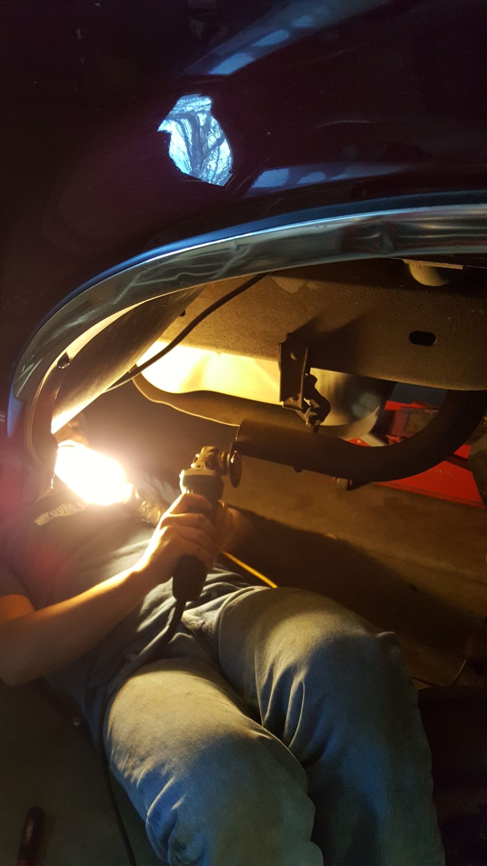 Person cutting exhaust pipe under a vehicle with an angle grinder