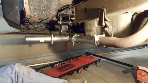 1996 Ford Bronco - Close-up view of a vehicle's exhaust system undergoing repair, with a mechanic's creeper visible below.