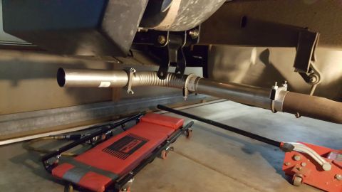 1996 Ford Bronco - Underbody view of an exhaust system repair, showing a flexible pipe section and clamps, with a creeper and jack visible.