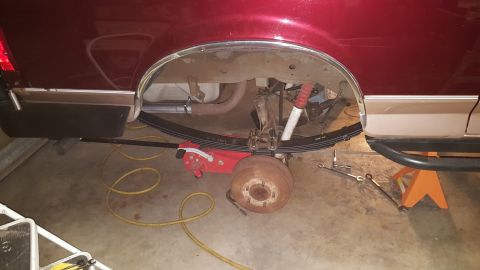 1996 Ford Bronco - The rear suspension of a red SUV is visible, with leaf springs and a shock absorber being worked on.