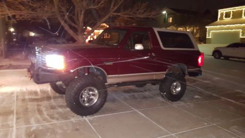 1996 Ford Bronco - Maroon Ford Bronco with lifted suspension and aftermarket wheels parked on a snowy driveway at night.
