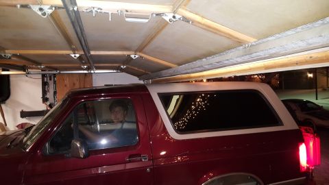 1996 Ford Bronco - A red Ford Bronco with a white top is parked inside a garage, with another vehicle visible outside.