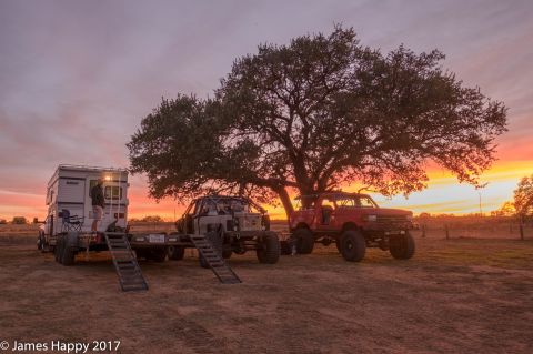 1989 Ford Bronco - A scenic view of two modified off-road trucks and a trailer set against a vibrant sunset sky.