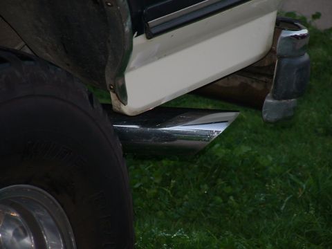 1990 Ford Bronco - A close-up view of a vehicle's exhaust pipe and rear bumper, with grass in the background.