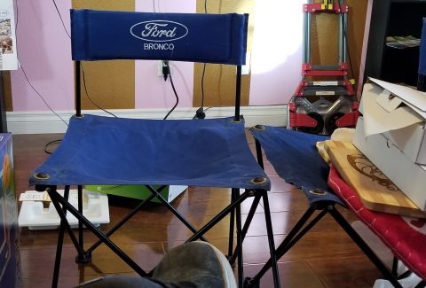 1967 Ford Bronco - Two blue folding chairs with the Ford Bronco logo are set up indoors, with other items in the background.
