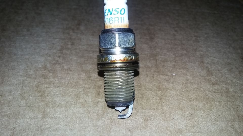 Spark plug with DENSO 16R11 text, showing wear and carbon buildup