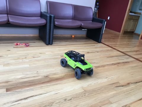 1989 Ford Bronco - A lime green remote control off-road vehicle sits on a polished wooden floor in front of burgundy chairs.