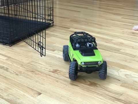1989 Ford Bronco - A remote-controlled rock crawler sits on a wooden floor, positioned near an open dog crate.