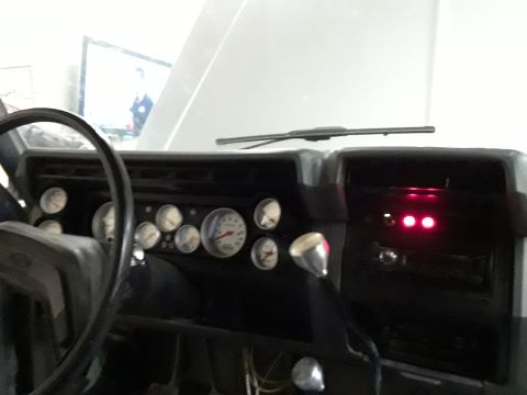1985 Ford Bronco - The dashboard displays numerous gauges and a chrome shifter, with two red indicator lights glowing.