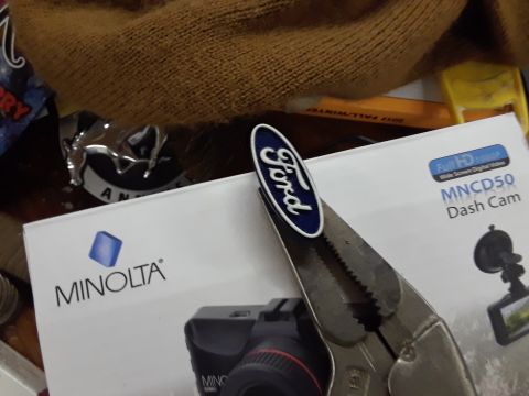 1985 Ford Bronco - A Ford emblem is held by pliers above a box for a Minolta dash cam.