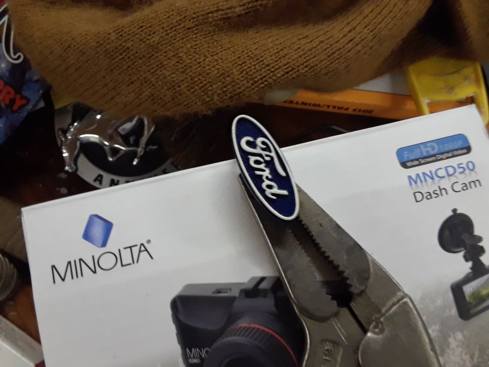 Pliers holding a Ford emblem over a box for a dash cam