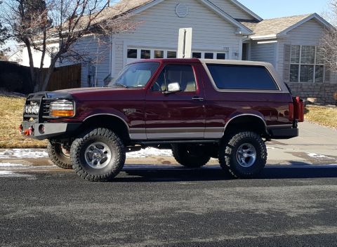 1996 Ford Bronco - A maroon 1996 Ford Bronco is shown from the side, modified with off-road tires and a custom bumper.
