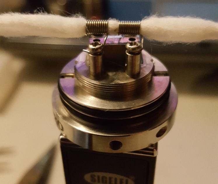 Close-up of a vape coil with cotton wicks, metal construction, on a black device