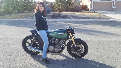 1976 Kawasaki KZ650-B2 - A person sits on a green cafe racer motorcycle parked on a street in front of a suburban house.