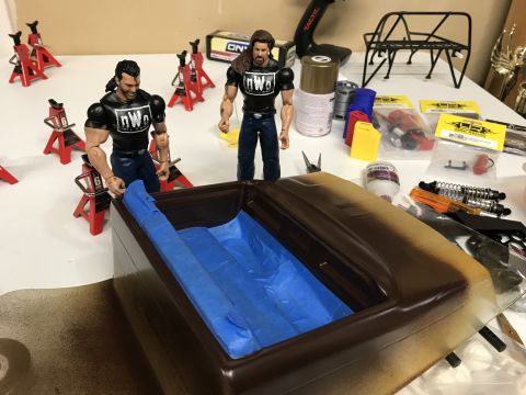1989 Ford Bronco - A collection of toy wrestling figures and parts for an RC car build are laid out on a workbench.