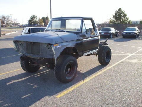 1978 Ford Bronco - A project 1978 Ford Bronco shown from a 3/4 front angle in a parking lot, with primer-gray front fenders and hood, a black cab and removed…