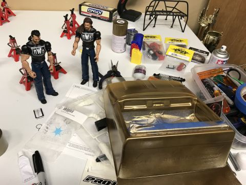 1989 Ford Bronco - A collection of RC car parts, tools, and action figures are laid out on a workbench, suggesting a hobbyist's project.