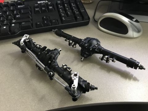 1989 Ford Bronco - Two detailed RC car axles are laid out on a desk, ready for assembly or modification.