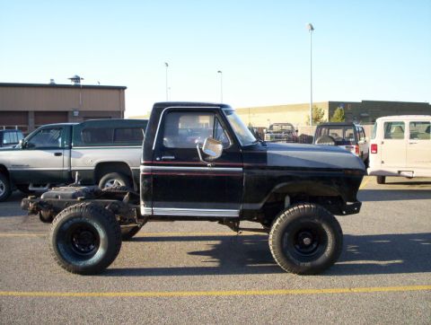 1978 Ford Bronco - A black 1978 Ford Bronco shown in side profile, lifted on large off-road tires with black steel wheels, and its rear bed/frame appears bare…