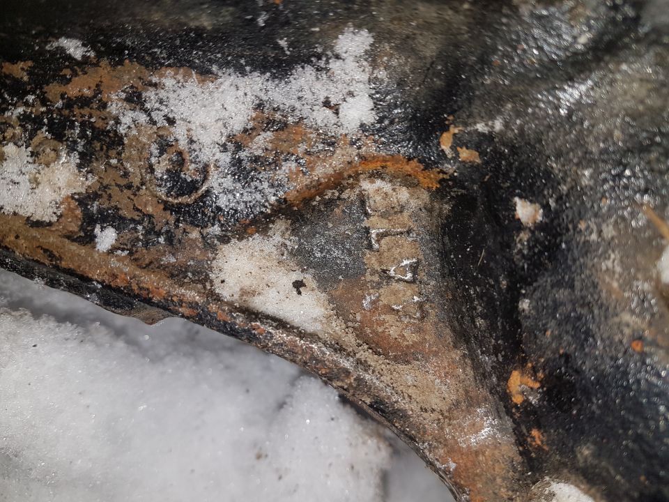 Close-up of a rusted metal casting with the partial text 'L4' visible, covered in snow