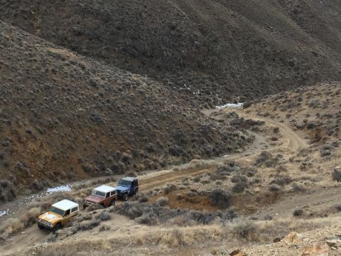 1969 Ford Bronco - Three 1969 Ford Broncos navigate a dirt road through a , arid terrain.