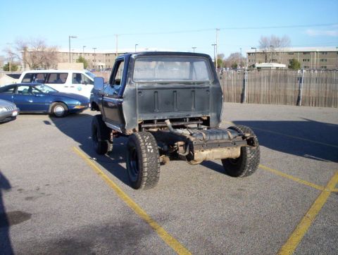 1978 Ford Bronco - A black pickup truck chassis is parked in a lot, with other vehicles nearby.