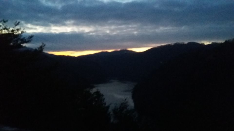 Mountains and a body of water under a cloudy sky at dusk. A yellow glow is visible on the horizon